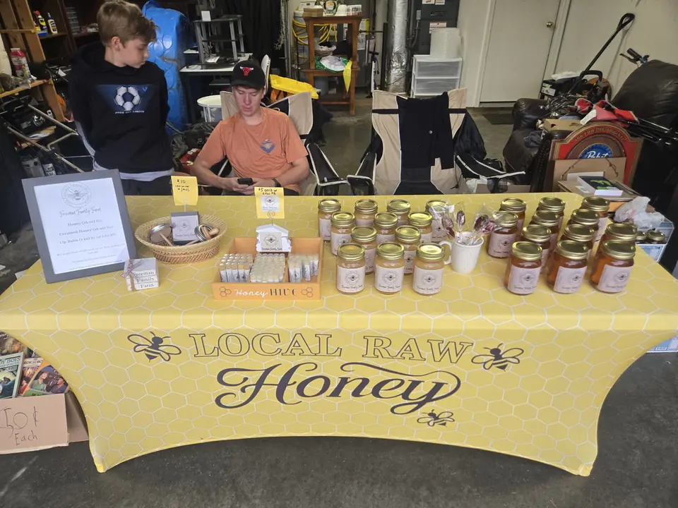 Two boys standing behind a table of honey jars and lip balm