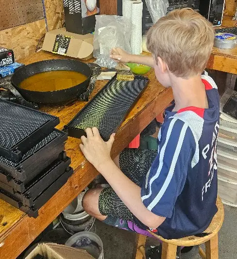 A young member of the Freeman family brushing wax onto new hive frames