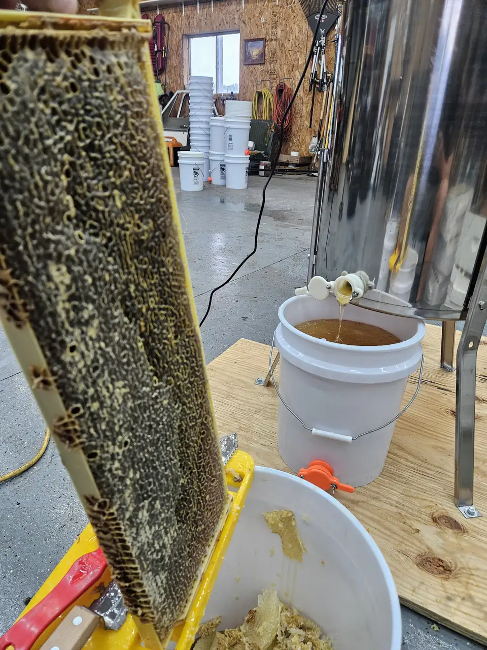 A honeycomb frame beside an extractor draining honey into a bucket
