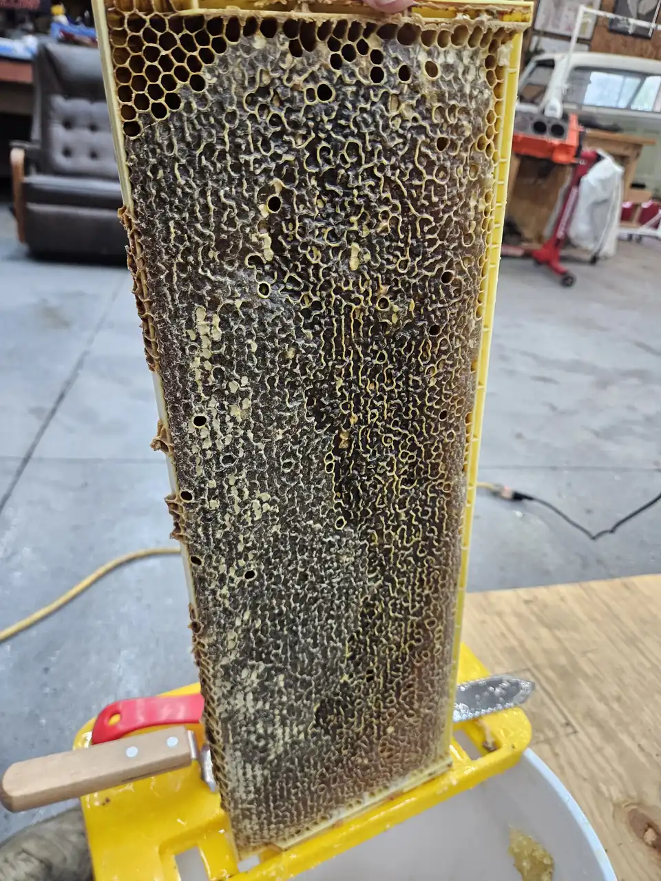 A honeycomb frame held upright beside the honey extractor